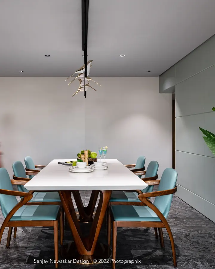 The Cladded House: a white dining table with blue upholstered chairs under a sculptural pendant.