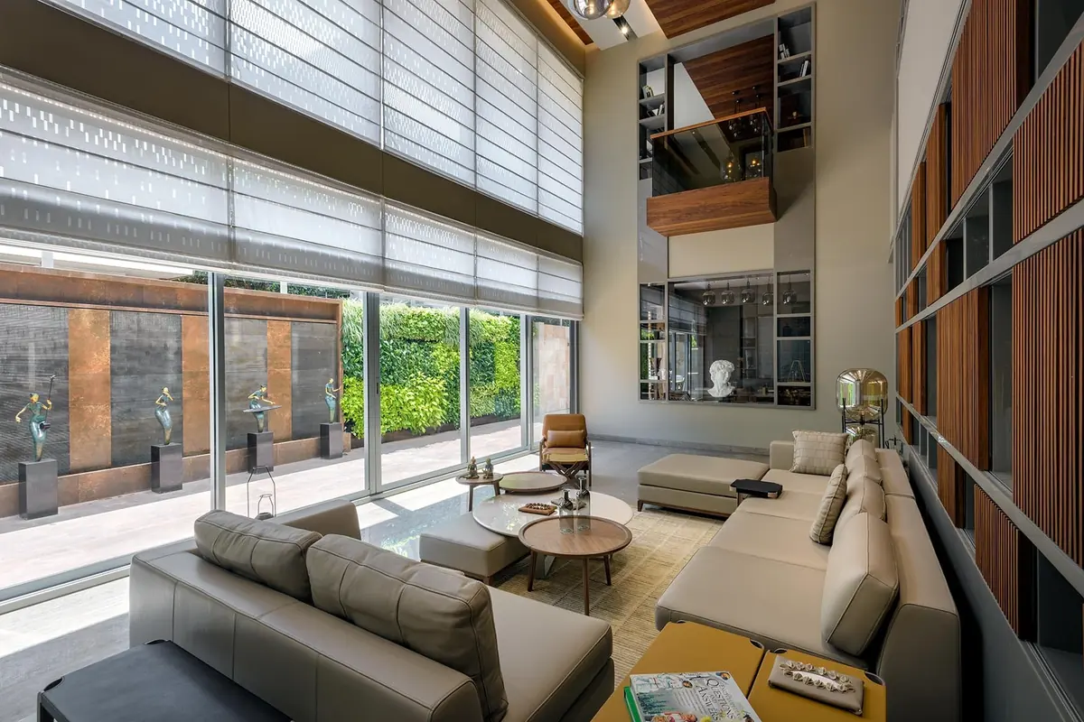 Cutting Edge House: a double-height living room with linen blinds, tall timber shelving and a view of the garden.
