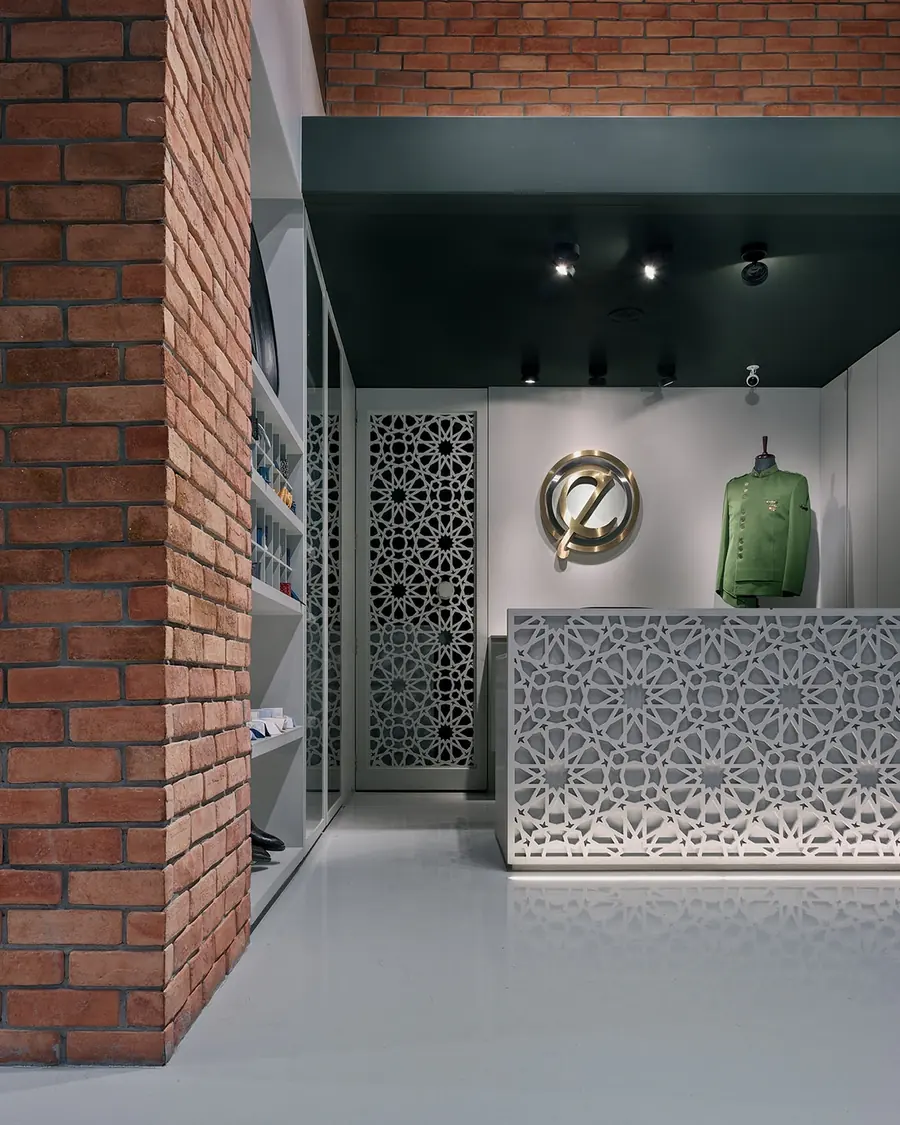 Ethaza menswear boutique: exposed brick, a perforated white jali screen and a backlit reception counter.