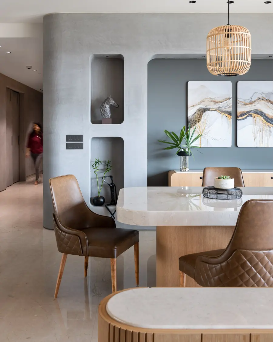Round Edges House: a dining table under a woven pendant, set against a grey wall with round-cornered niches.